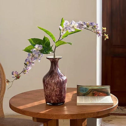 Glass flower vase with purple flowers on round wooden table